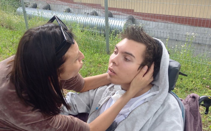 Kobieta przytula mężczyznę na wózku inwalidzkim.