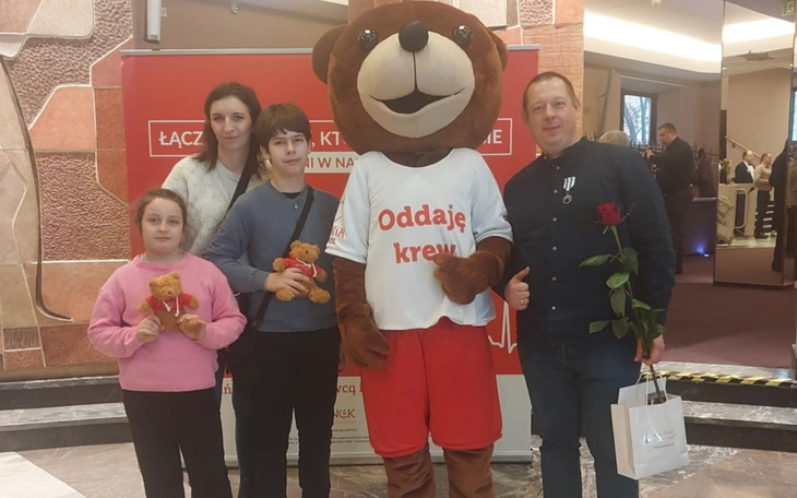 Rodzina z maskotką misia promującego oddawanie krwi.