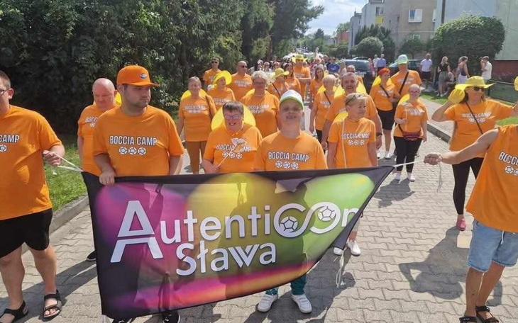 Ludzie w pomarańczowych koszulkach podczas marszu z transparentem.