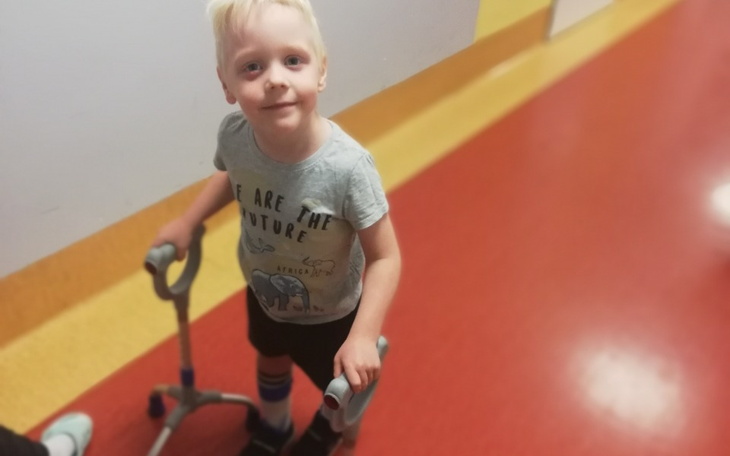 Chłopiec z chodzikiem, uśmiechający się na korytarzu.