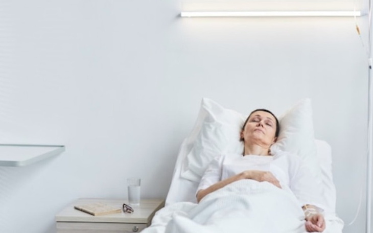 Kobieta leży w łóżku szpitalnym, z zamkniętymi oczami.