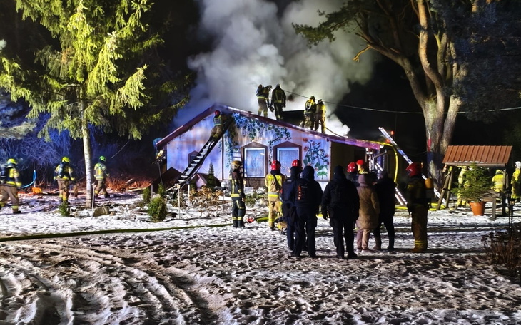 Strażacy gaszący pożar w domku, otoczeni dymem i śniegiem.