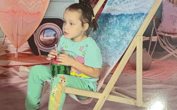 Mała dziewczynka siedząca na leżaku, rysująca w letniej scenerii.