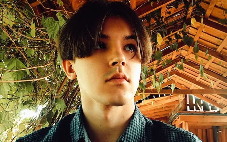 Młody mężczyzna z długimi włosami, patrzy w dal w otoczeniu zieleni.