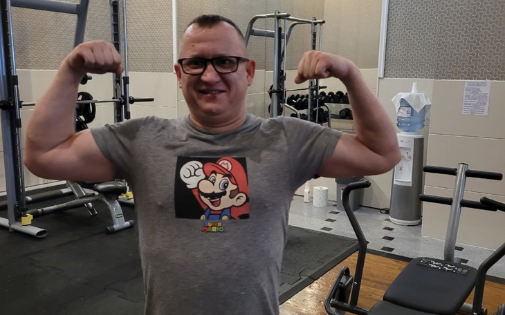 Mężczyzna w koszulce z Mario, pokazujący mięśnie na siłowni.