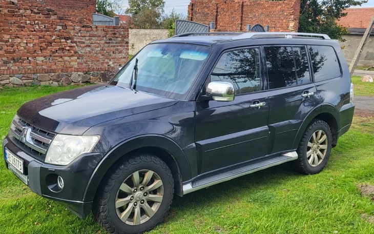 Czarny SUV zaparkowany na trawie, w tle ceglana ściana.