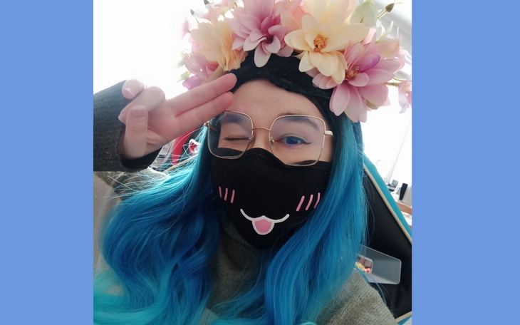 Osoba w masce z kwiatami na głowie, robiąca znak pokoju.