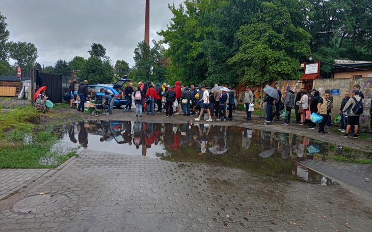 Ludzie w kolejce w deszczu, odbicie w kałuży.