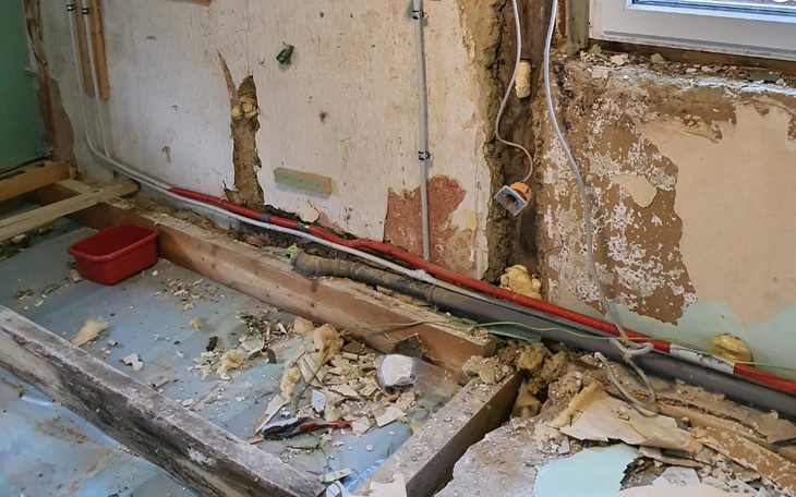 Uszkodzona ściana z widocznymi rurami i odpadami budowlanymi.