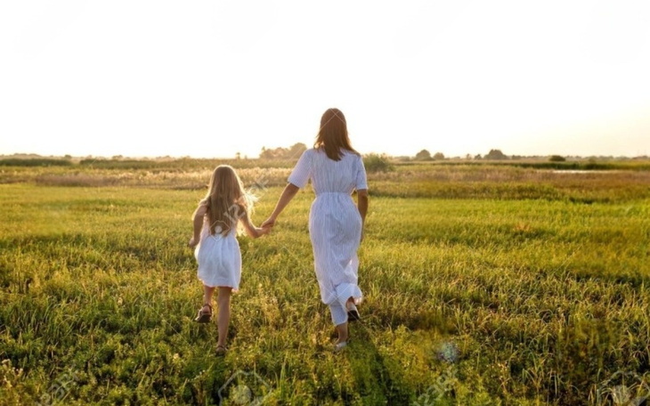 Matka z córką spacerują po zielonym polu w promieniach słońca.