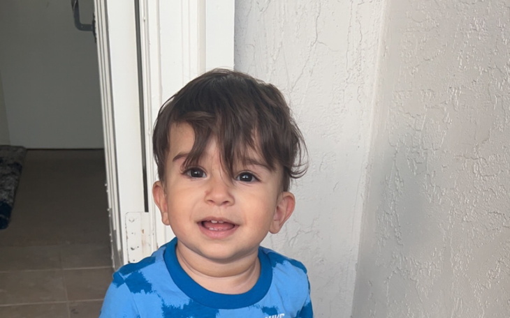 Mały chłopiec w niebieskiej koszulce, uśmiechający się w drzwiach.