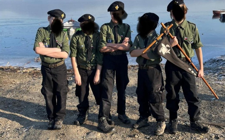 Grupa dzieci w mundurach, pozująca nad wodą.
