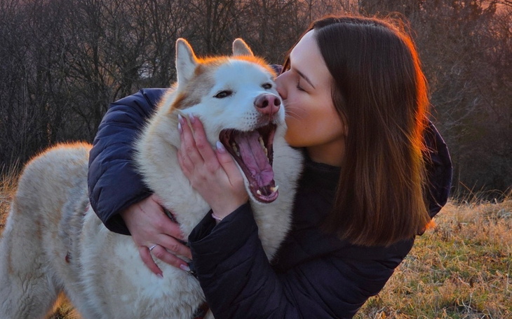 Kobieta przytulająca psa na tle zachodzącego słońca.