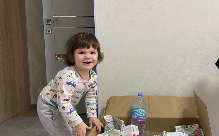 Małe dziecko bawi się w kartonowym pudle, uśmiechnięte.