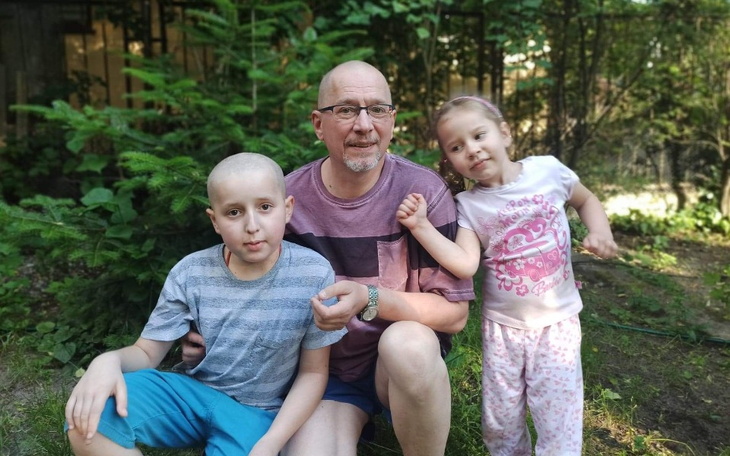 Dzieci z dorosłym w ogrodzie, uśmiechnięte i radosne.