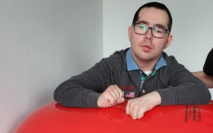 Mężczyzna z okularami siedzi przy dużej czerwonej piłce.