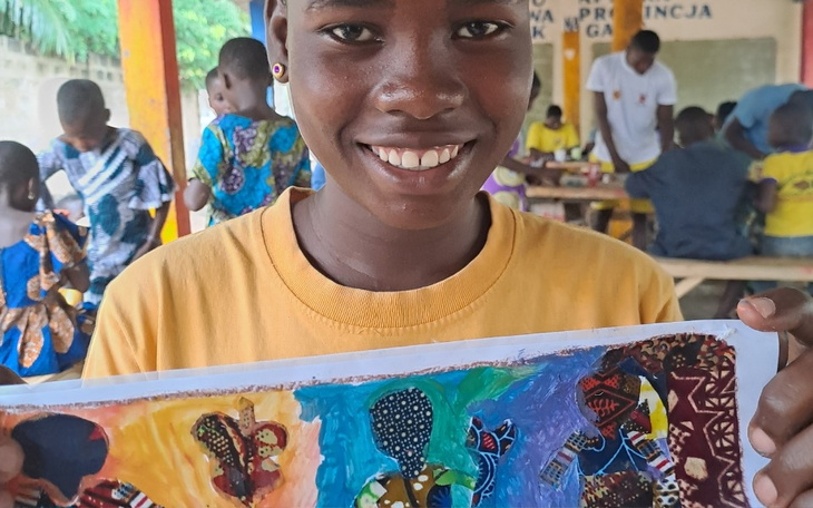 Chłopiec trzymający rysunek, uśmiechający się do kamery.