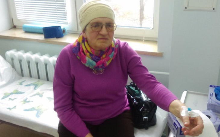 Starsza kobieta w szaliku, siedząca w szpitalu.