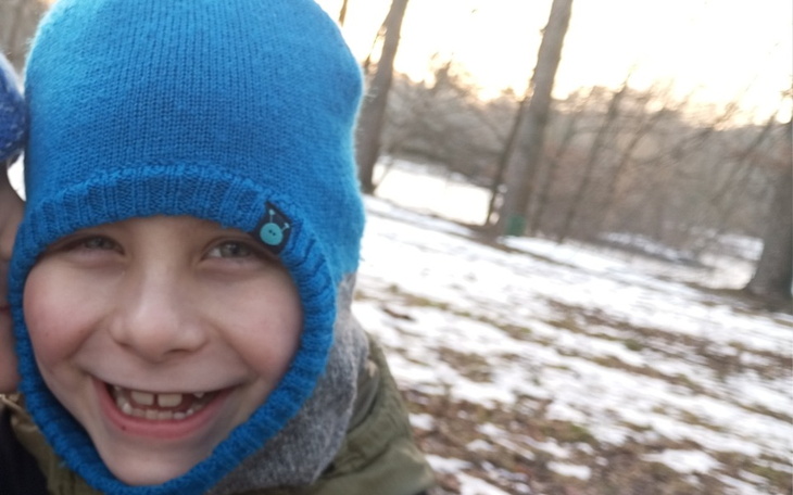 Chłopiec w niebieskiej czapce, uśmiechający się na tle lasu.