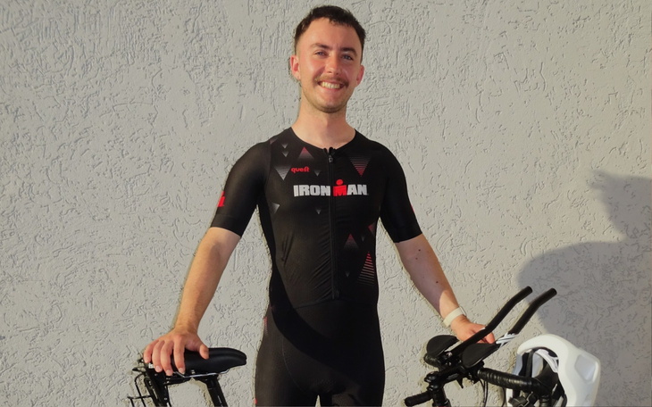 Młody mężczyzna w stroju triathlonowym, uśmiechający się z rowerem.