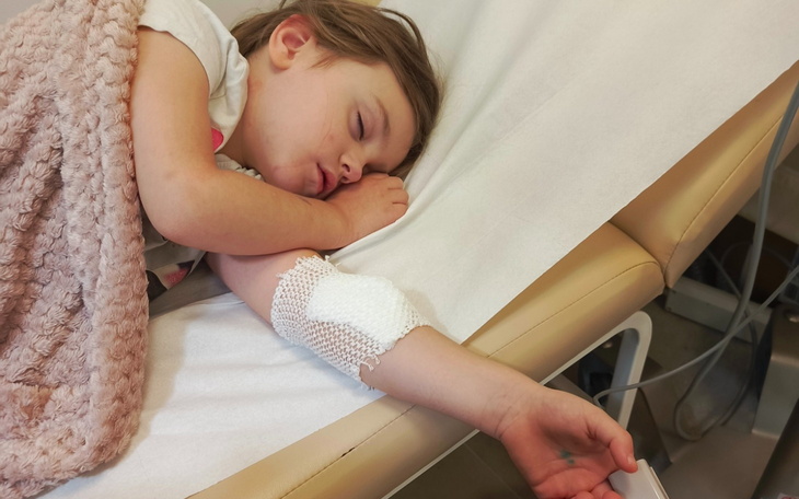 Mała dziewczynka śpi na łóżku, z opatrunkiem na ręce.