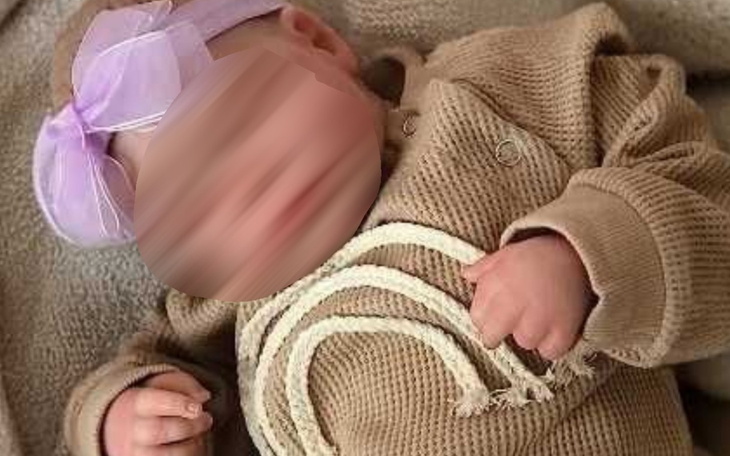Małe dziecko w sweterku z tęczą, z różową kokardą.