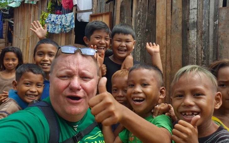 Grupa dzieci uśmiecha się i macha do kamery, radosna atmosfera.