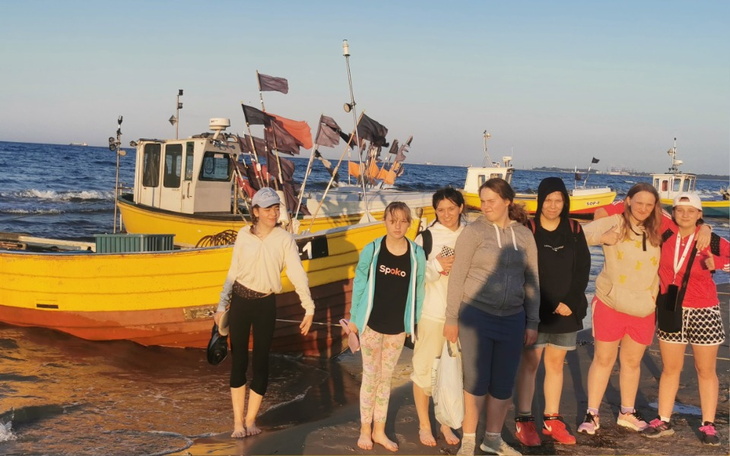 Grupa osób na plaży obok kolorowych łodzi rybackich.