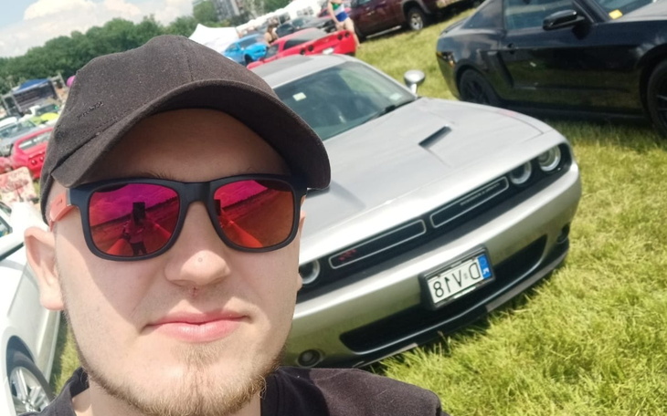 Mężczyzna w okularach przeciwsłonecznych przy samochodzie na zlocie.