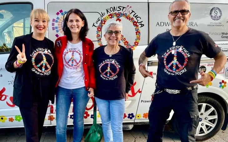 Cztery osoby w koszulkach z symbolem pokoju, uśmiechają się do kamery.