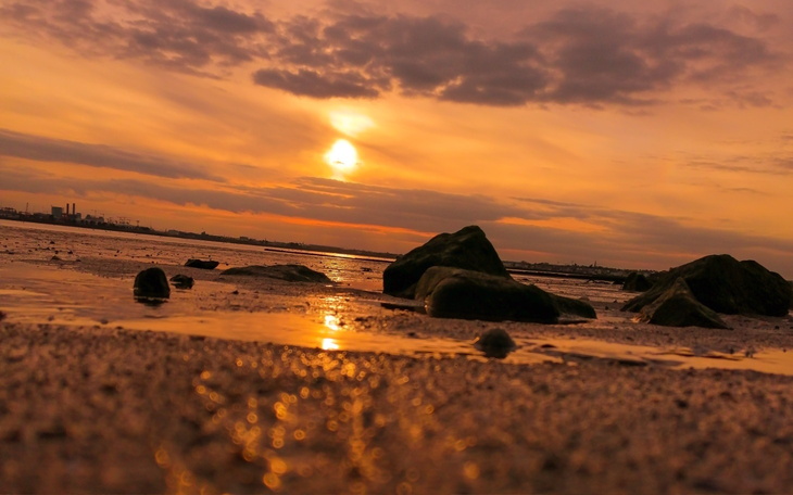Zachód słońca nad brzegiem morza z kamieniami na plaży.
