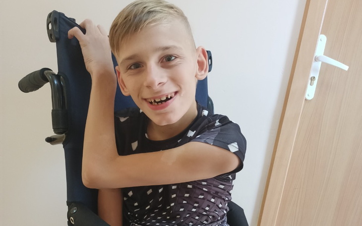 Uśmiechnięty chłopiec w wózku, z radością na twarzy.