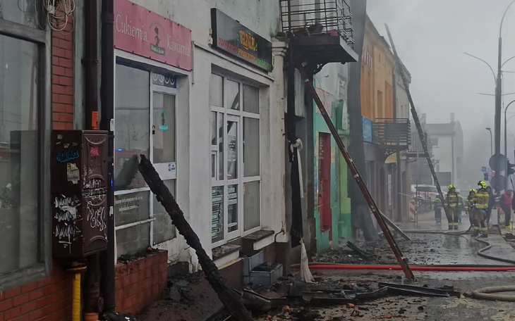 Zniszczona ulica po pożarze, strażacy w tle.