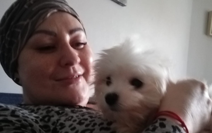 Kobieta trzymająca małego psa, obie uśmiechnięte.