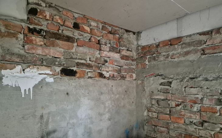 Fragment ściany z odsłoniętymi cegłami i tynkiem.