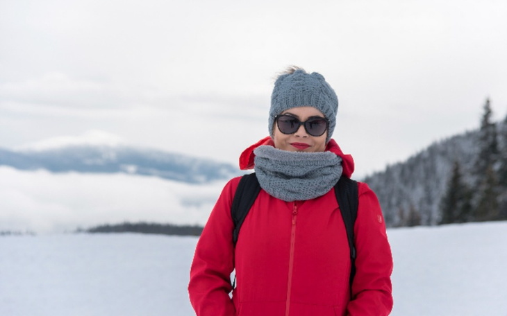 Kobieta w czerwonym płaszczu na tle gór w zimie.