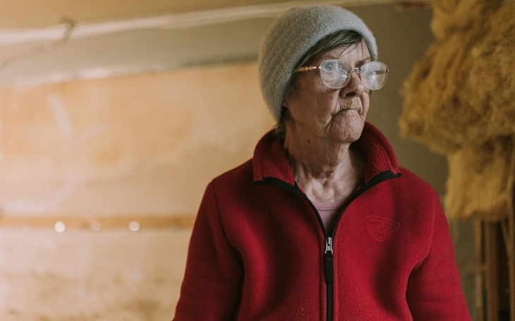 Starsza kobieta w czerwonym swetrze, z okularami, w pomieszczeniu.