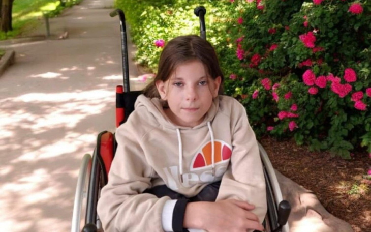 Dziewczynka w wózku inwalidzkim na tle kwiatów.