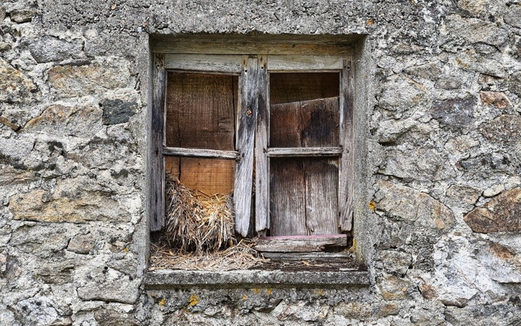 Stare okno w kamiennej ścianie z widoczną słomą.