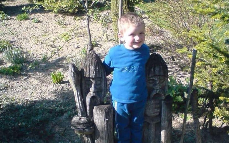 Chłopiec pozujący obok drewnianych rzeźb w słonecznym ogrodzie.