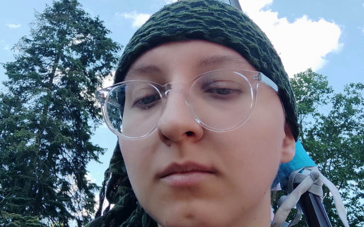 Osoba w okularach, z zielonym szalikiem, na tle drzew.