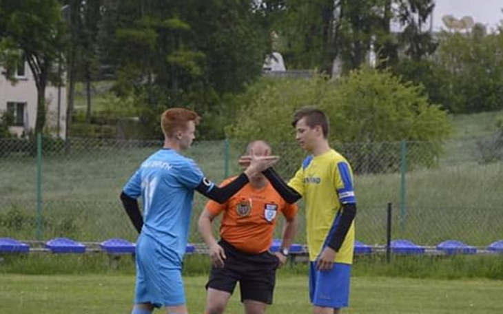 Młodzi piłkarze rozmawiają z sędzią na boisku.