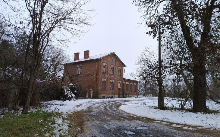 Stary budynek w zimowym krajobrazie, otoczony drzewami.