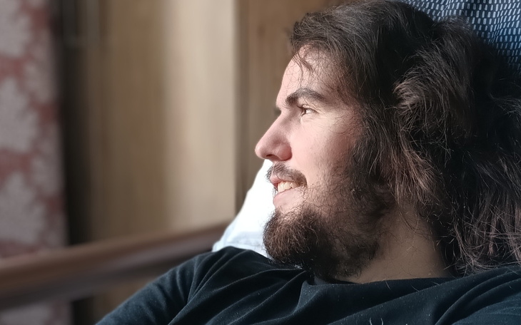 Mężczyzna z długimi włosami uśmiechający się w świetle dziennym.