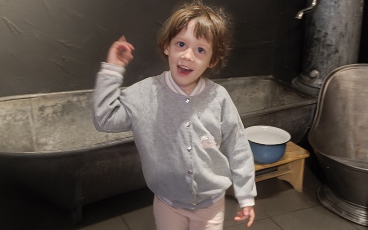 Mała dziewczynka w szarej bluzie, uśmiecha się i wskazuje palcem.