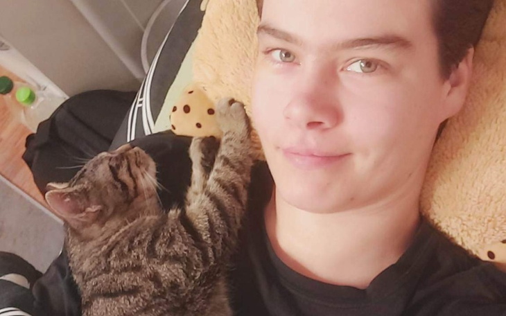 Młody człowiek z kotem na rękach, oboje wyglądają na szczęśliwych.