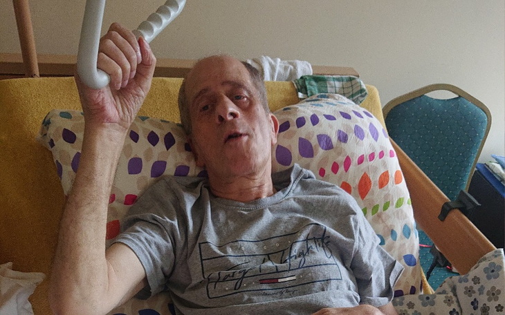 Mężczyzna leżący na łóżku szpitalnym, z ręką uniesioną w górę.