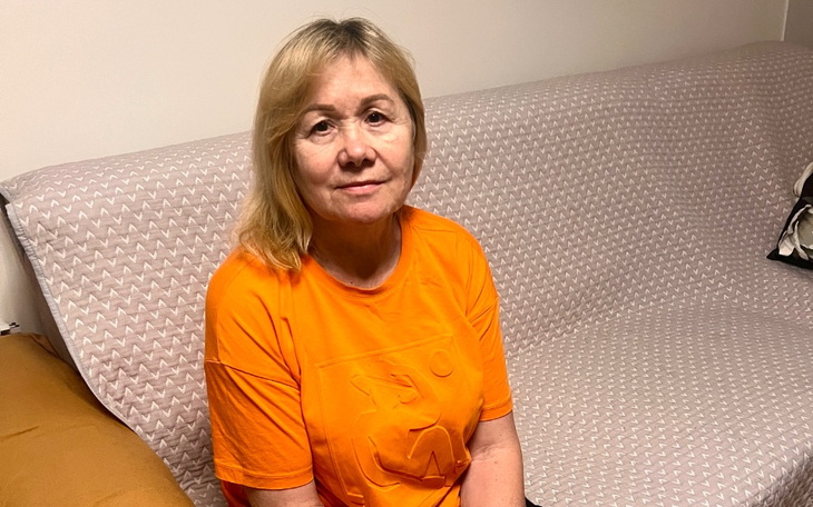 Kobieta w pomarańczowej koszulce siedzi na kanapie.