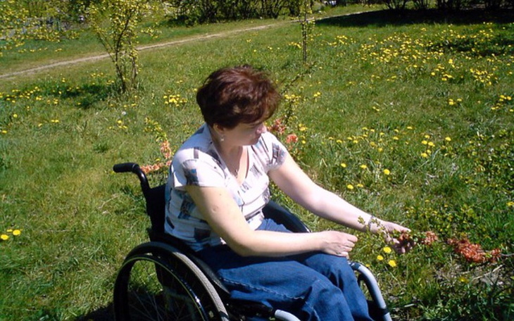 Kobieta na wózku inwalidzkim, zbierająca kwiaty w ogrodzie.