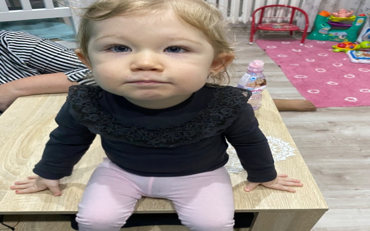 Mała dziewczynka siedząca na stole, z poważnym wyrazem twarzy.